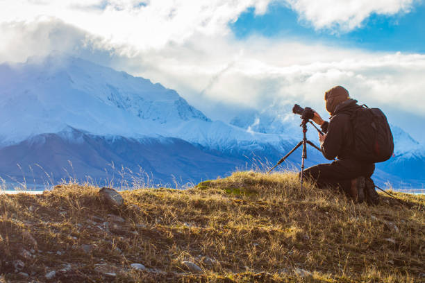 istock Young professional man operating camera equipment on tripod setup taking photographs of dramatic mountain landscape 1497731914