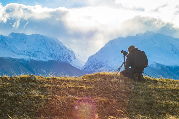 istock Young professional man operating camera equipment on tripod setup taking photographs of dramatic mountain landscape 1497731922