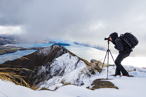 Cold winter theme of male professional photographer taking photographs of snow covered mountains. Photographed in New Zealand.