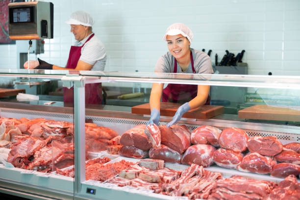 young female seller shows demonstrates raw beef ribs in glass showcase of refrigerator. - butchers shop imagens e fotografias de stock