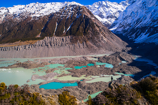 Nature scene of man looking out over multi-coloured moraine landscape with bright blue glacial melt pools in New Zealand.