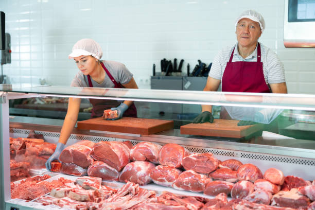 istock Elderly butcher shop owner standing behind display case with meat 1497732104