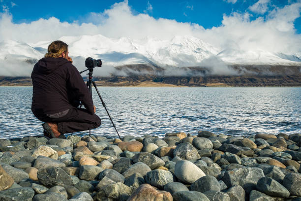 istock Young professional man operating camera equipment on tripod setup taking photographs of dramatic mountain landscape 1497732199