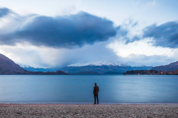 istock Man standing looking out over lake scene in winter with dramatic landscape and clouds 1497732413