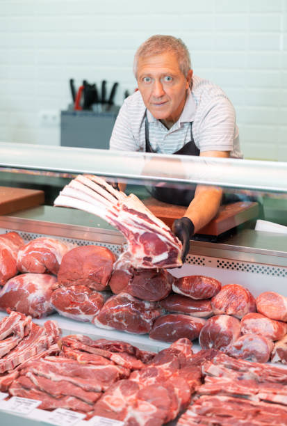 istock Positive elderly salesman in apron and disposable gloves shows raw beef tomahawk steak 1497732437