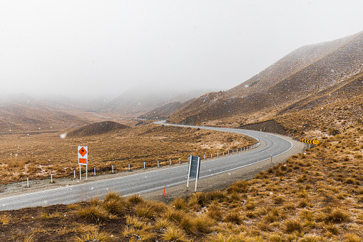 Road-trip theme of country road winding through snow covered mountain background in misty overcast conditions. Photographed in New Zealand.