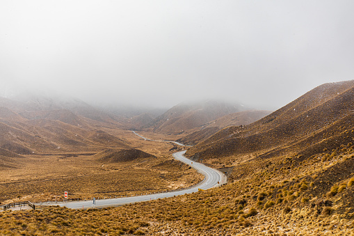 Road-trip theme of country road winding through snow covered mountain background in misty overcast conditions. Photographed in New Zealand.