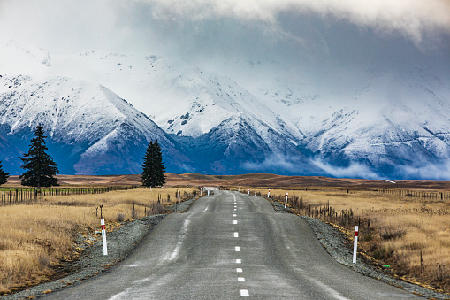 Road-trip theme of road diminishing into dramatic ethereal snow covered mountain background. Photographed in New Zealand.