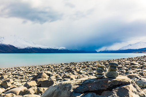 Lake shore scene in winter with rocks and dramatic mountain landscape and clouds in New Zealand.