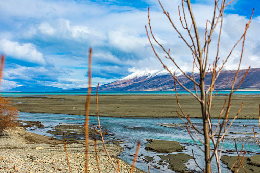 Turquoise lake and braided river with dramatic landscape of snow capped mountains in background, shot in New Zealand.