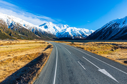 Road-trip theme of road curving toward dramatic snow covered mountains. Photographed in New Zealand.