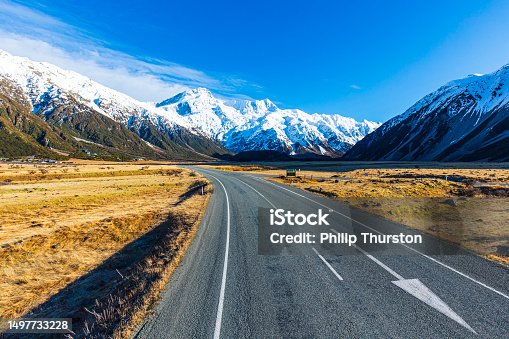istock Road-trip theme of road curving toward dramatic snow covered mountains 1497733228