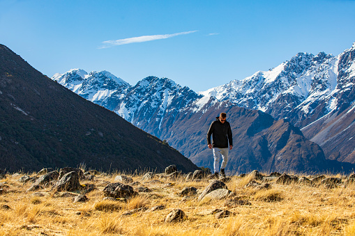 Adventure theme of young man hiking in nature walking with snow covered mountains. Photographed in New Zealand.