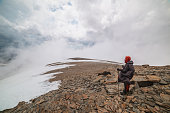 Awesome minimalist mountain landscape with hiker at very high altitude in dense low clouds. Wonderful alpine scenery with man on stone hill with snow in thick clouds. Man and majestic mountains nature