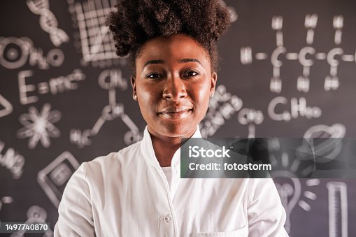 istock Portrait of charming female scientist standing in front of a blackboard with chemistry formulas. smiling at camera 1497740870