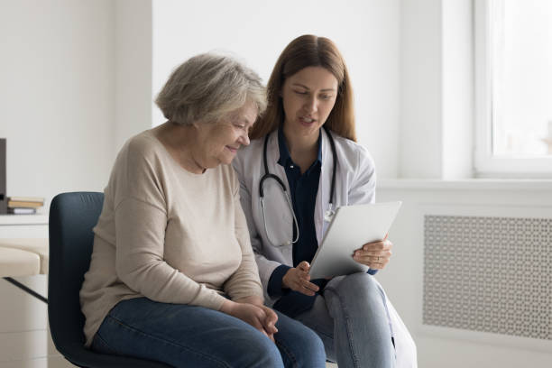 Positive engaged geriatrician doctor showing medical checkup result on tablet stock photo