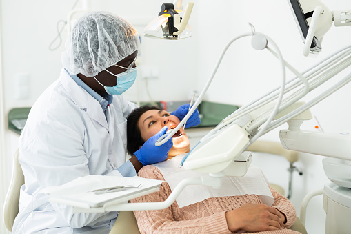 African american dentist is treating female patient which is sitting in dental chair