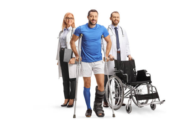 full length portrait of a male athlete with crutches and a walking brace standing in front of doctors - physical injury men orthopedic equipment isolated on white imagens e fotografias de stock