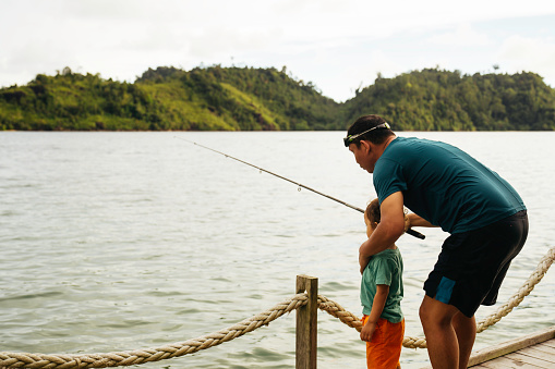 Shot of a father helping his son to reel in a fish
