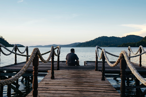 A man sitting at the edge of a jetty at sunset in terusan mande, painan, west sumatra