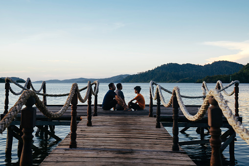 asian man sitting at the edge of a jetty at sunset in terusan mande, painan, west sumatra