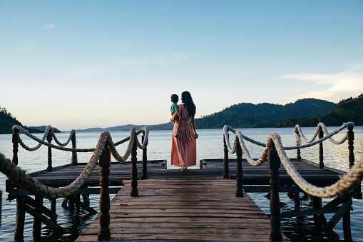 asian mother carrying son on jetty at sunrise, in terusan mande, painan, west sumatra
