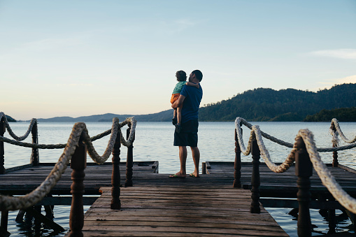 father carrying son on jetty at sunrise, in terusan mande, painan, west sumatra