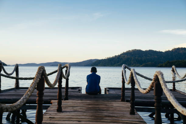 istock man sitting on a wooden footbridge at sunset 1497763556
