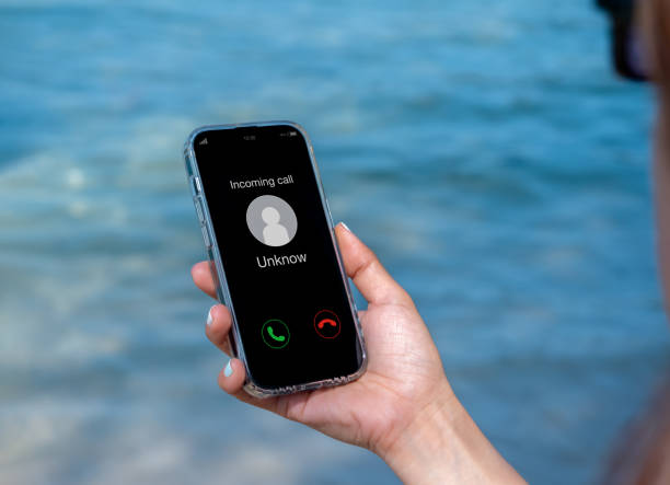 istock Incoming call with unknown caller, malicious phone calls concept. Unknown number displayed showing on smart mobile phone in woman hand on leave day at the beach. Spam and robocalls, scam call alert. 1497763558