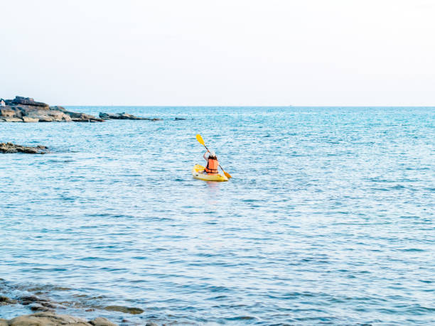 спина азиатской женщины в спасательном жилете и кепке, плывущей на желтой байдарке с веслом по морю. счастливая женщина, развлекающаяся на � - women kayaking life jacket kayak стоковые фото и изображения