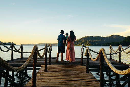 Asian couple carrying son on jetty at sunrise, in terusan mande, painan, west sumatra