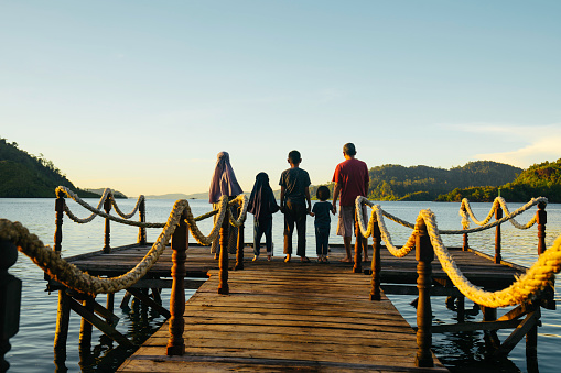 Asian couple with their children on jetty at sunrise, in terusan mande, painan, west sumatra