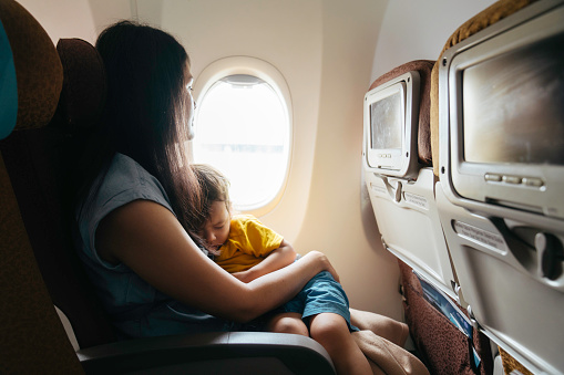 Baby sleeps in mom's arms while on an airplane in flight.