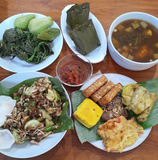 Indonesian Sundanese food - A selection of Sundanese foods from West Java including karedok, sayur asem, steamed tofu, lalapan steamed vegetables, tempe goreng, tempe mendoan, tahu goreng, empal gepuk, ayam goreng and a small dish of red chilli sambal all presented on a teak wood table top. comida sundanesa indonesia - una selección de alimentos sundaneses de java occidental incluyendo karedok, sayur asem, tofu al vapor, verduras al vapor lalapan, tempe goreng, tempe mendoan, tahu goreng, empal gepuk, ayam goreng y un pequeño plato de chile