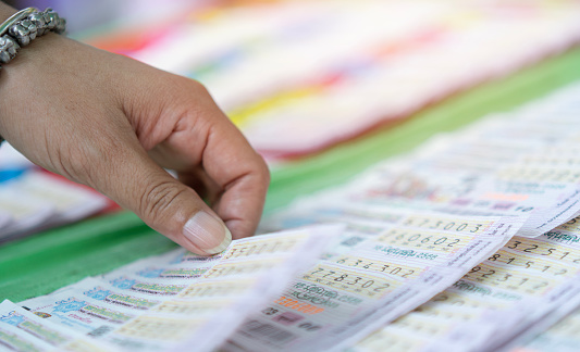 Asian woman hand holds of choose pile of Thailand lottery in blur bright sunlight. Close up, selective focus.