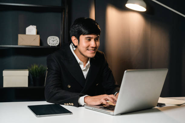 istock Young asian businessman working with laptop computer in the dark office at night. Attractive handsome Indian man work hard overtime in home with floor lamp ambient warm light late at night 1497776247