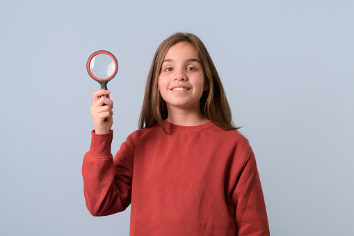 Portrait of girl with a magnifying glass. Red sweater, light blue background