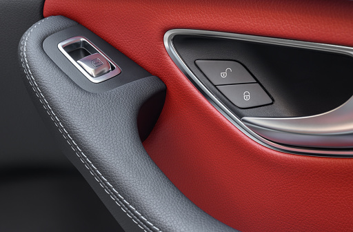 Close up of door lock and power window buttons in a modern car with red leather interior.
