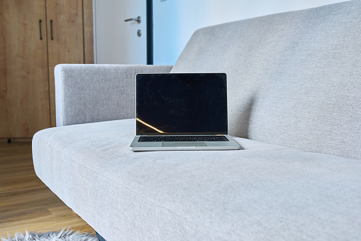 Open laptop on a modern gray sofa in the interior, background. Technology, work, study, freelance, leisure, lifestyle concept