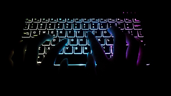A man typing using colorful glowing keyboard in the dark room