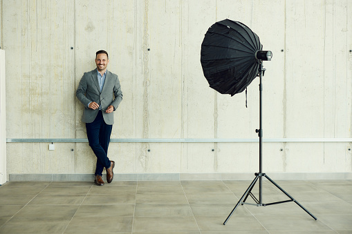 Happy businessman standing against the wall in a photo studio and looking at camera. Copy space.