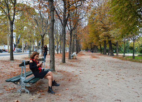 Paris, France - Oct 3, 2018. Unknown young woman resting on the bench at tree park near Arc de Triomphe of Paris.