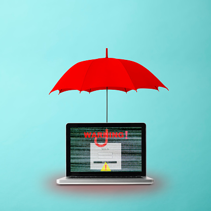 Close-up of laptop with warning sign protected by red umbrella on light blue background with copy space.