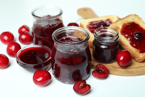 Cherry jam sandwiches and ingredients on white background