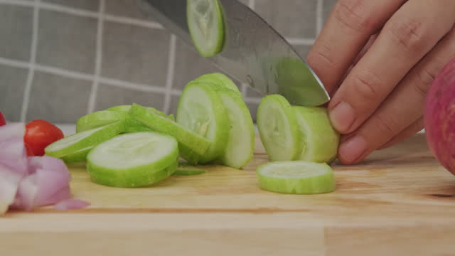 Female hand using a knife to slice cucumbers on a cutting board. Close-up. Woman with kitchen knife cutting cucumber at home. Preparing homemade food