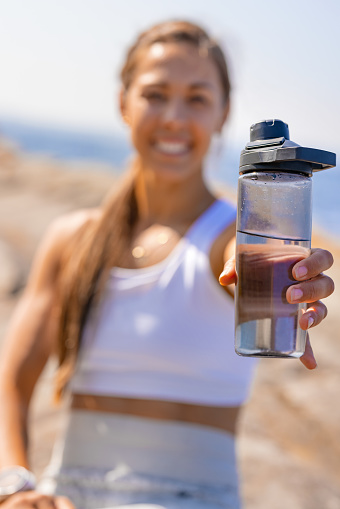 Portrait of smiling fit athletic woman holding water bottle and taking break during outdoor workout