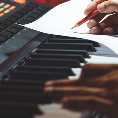close up songwriter hand writing a hit song on music sheet while playing piano. song writing concept