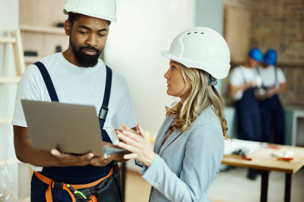 istock Female architect and black manual worker using laptop in moving apartment. 1497799206