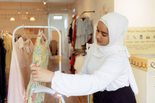 Young Malay Muslim Woman Business Owner Steaming Clothes in Local Thrift Fashion Shop stock photo