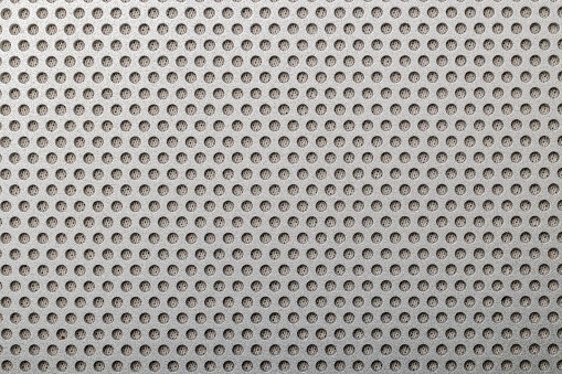 Closeup shot of metallic grill of a speaker featuring an array of small holes for sound output